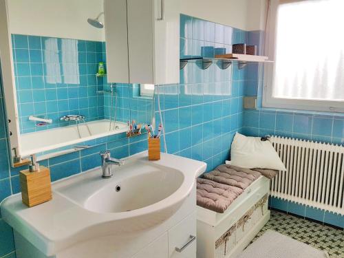W wyłożonej niebieskimi kafelkami łazience znajduje się umywalka i wanna. w obiekcie Haus am Bodensee w mieście Fußach