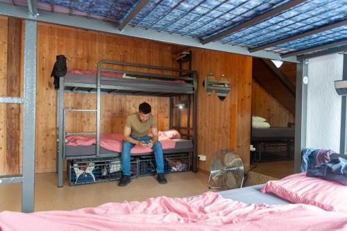 a man sitting on a bed in a room with bunk beds at Balmers Hostel in Interlaken