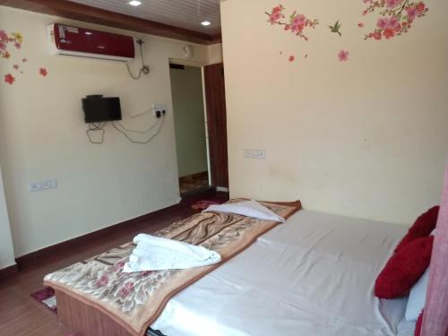 um pequeno quarto com uma cama com lençóis brancos e flores na parede em New natraj em Chikalda