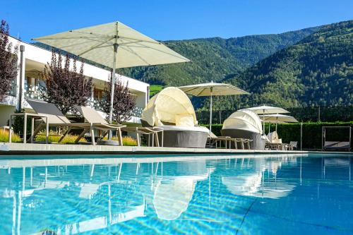 a swimming pool with chairs and umbrellas in front of a building at Residence & Sportlodges Claudia in Plaus