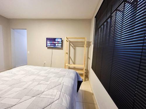 Espaço BlauHaus próximo a Vila Germânica في بلوميناو: غرفة نوم مع سرير وتلفزيون على الحائط