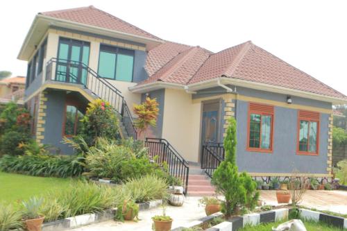 une maison avec une terrasse couverte et un toit dans l'établissement Alice Gardens and Campsite, à Entebbe