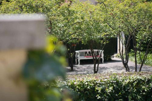 a white bench in a park with trees and bushes at Hotel am Schlosspark Zum Kurfürst in Oberschleißheim