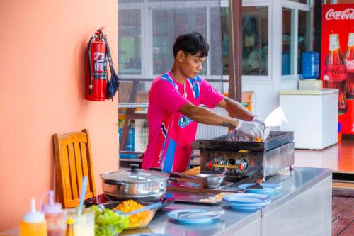 a woman preparing food on a grill in a kitchen at เดอะวอเตอร์ปาร์ครีสอร์ท- The Water Park Resort in Ban Laem Mong Khoi