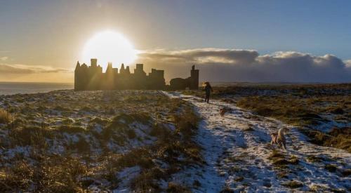 a person walking on a snowy field with a castle in the background at Room on the River in Cruden Bay
