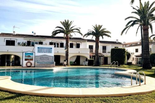- une piscine en face d'un bâtiment avec des palmiers dans l'établissement Adosado en Urbanización la Aldea Denia, à Dénia