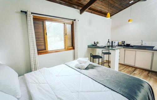 a white bedroom with a large bed and a kitchen at Chalé Mantiqueira in Cunha