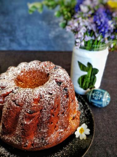 un gâteau de bundt sur une assiette à côté d'un vase de fleurs dans l'établissement Commanderie Cottage Colmar, à Colmar