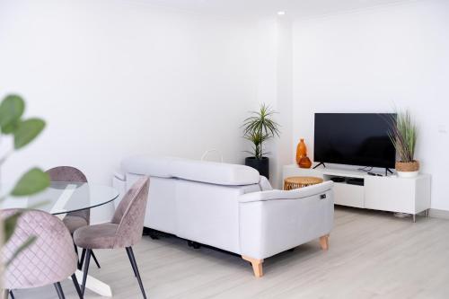 a white living room with a white couch and a tv at Sunset House over the Sea in Sesimbra