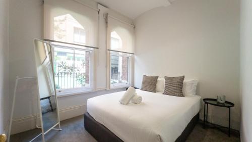 a bedroom with a large white bed with two windows at Gordon House Apartments in Melbourne