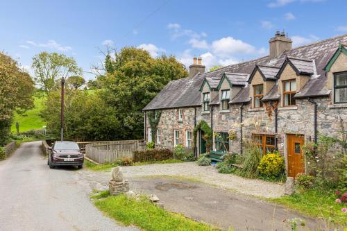 an old stone house with a car parked in the driveway at Priest Bridge Cottage in Bryansford