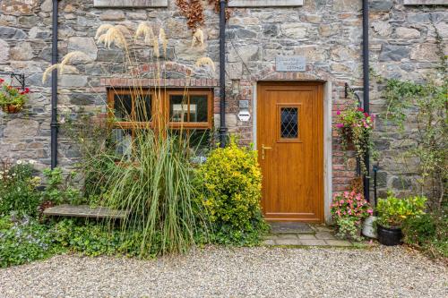 a stone house with a wooden door and some plants at Priest Bridge Cottage in Bryansford