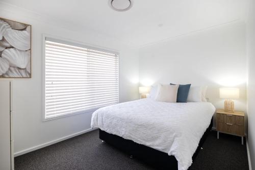 a white bedroom with a bed and a window at Coastal Breeze - 67 Burrill Street in Ulladulla