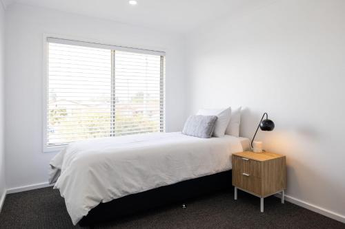 a white bedroom with a bed and a window at Coastal Breeze - 67 Burrill Street in Ulladulla