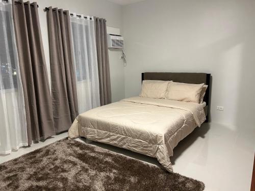 Cama en habitación blanca con cortinas y alfombra en Camella Manors Condo, IBIZA Bldg., en Bacolod
