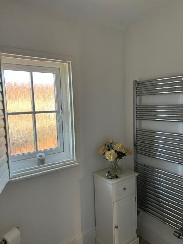 a bathroom with a window and a vase of flowers on a cabinet at LN Host in Hardingstone