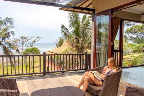 a woman sitting in a chair reading a book on a balcony at Beach Villa Balian in Selemadeg