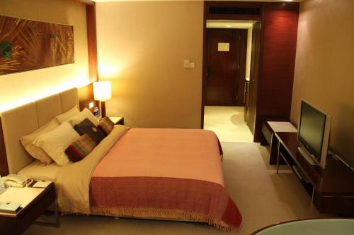 a hotel room with a bed and a flat screen tv at Dongguan Richwood Garden Hotel in Dongguan