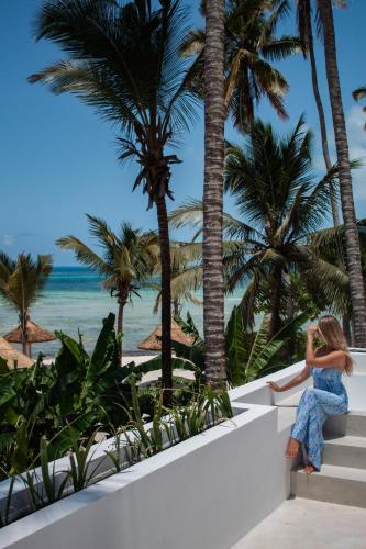 a woman sitting on a ledge looking at the beach at Ycona Eco-Luxury Resort, Zanzibar in Dikoni