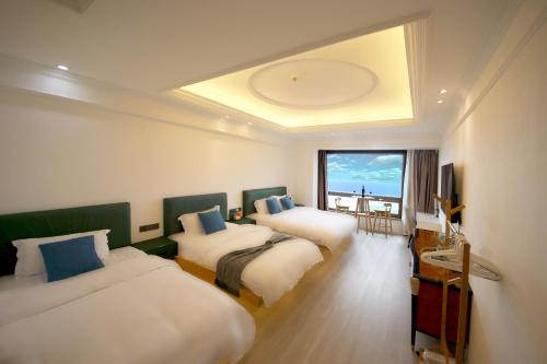 Habitación de hotel con 3 camas y ventana grande. en PingTan YuCheng Seaview Blue Smart Hotel, en Pingtan