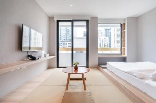 a bedroom with a bed and a table and windows at LiveZen Bangkok in Khlong Toei
