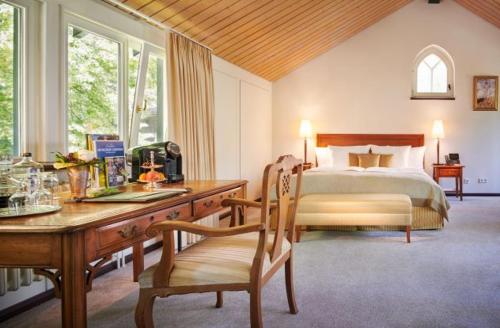 een slaapkamer met een bed en een bureau met een stoel bij Relais & Chateaux Hotel Hohenhaus in Herleshausen