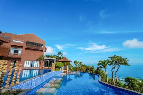 a swimming pool in front of a building with the ocean in the background at Yalong Bay Earthly Paradise Birds Nest Resort （Mountain Villas) in Sanya