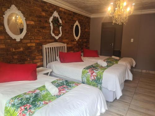 a room with three beds with white sheets and red pillows at Royal Villa Guesthouse in Brakpan