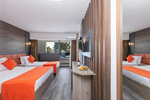 Maya World Didyma Hotel في ديديم: غرفة في الفندق بسريرين وملاءات برتقالية
