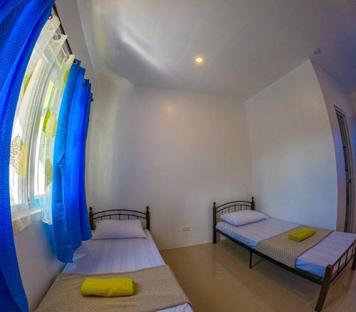 two beds in a room with a window and blue curtains at Divers Lodge Plumeria in Moalboal
