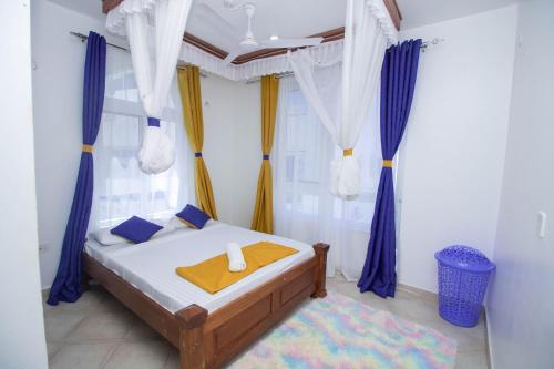 a bedroom with a bed with blue and yellow curtains at Kijani Suites in Malindi