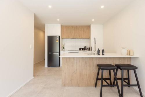 a kitchen with a black refrigerator and two bar stools at Inner City Luxury With Free Parking in Christchurch