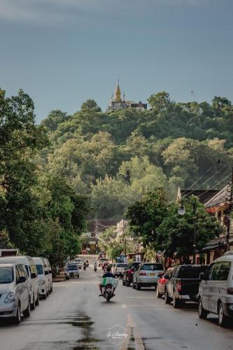 a person riding a motorcycle down a street with cars parked at QUEEN'S HOUSE in Luang Prabang