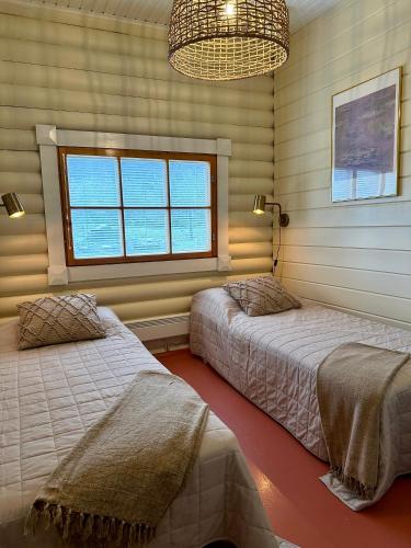 two beds in a bedroom with a window and a chandelier at Kuusiston majatalo in Kuusisto