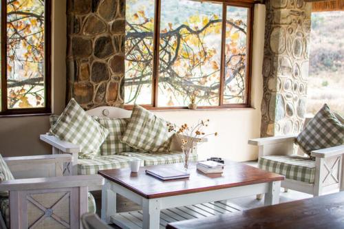 a living room with a couch and a table and windows at Lolambazo Country House & Cottage - Giants Castle Drakensberg in Mahlutshini