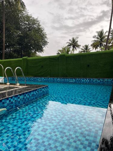 una piscina azul con una valla y palmeras en The Terra Hotel North Goa 