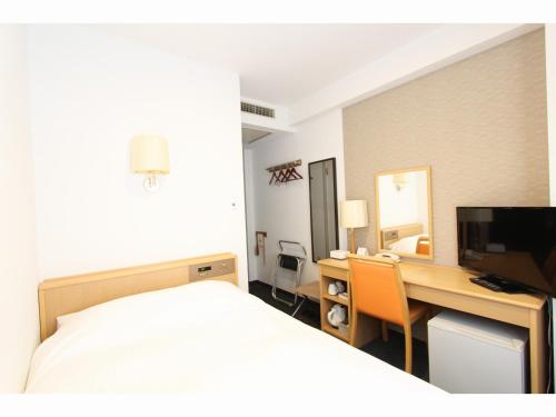 a hotel room with a bed and a desk with a television at Smile Hotel Yonezawa in Yonezawa