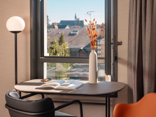 a table with a vase and a window with a book at Novotel Orléans Centre Gare in Orléans