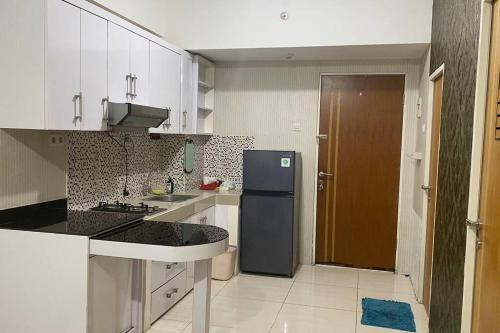 eine Küche mit einem schwarzen Kühlschrank und weißen Schränken in der Unterkunft Puncak Bukit Golf Apartemen in Surabaya