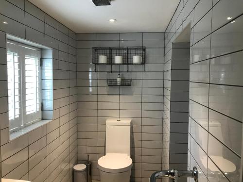 Łazienka wyłożona jest białymi kafelkami i dysponuje toaletą oraz oknem. w obiekcie Angel Cottage Cozy Nook w mieście Boxgrove