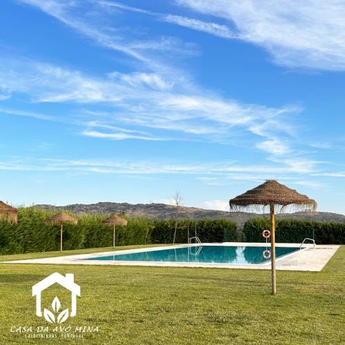 a swimming pool with a straw umbrella in the grass at A casa da avó Mina in Sortelha