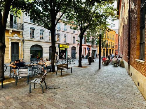 Une rue de la ville avec des gens assis à des tables et des bancs dans l'établissement L’Esquile Rose - Charmant studio en hypercentre, à Toulouse