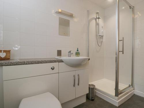 a white bathroom with a sink and a shower at Roan Cottage in Lydiard Millicent
