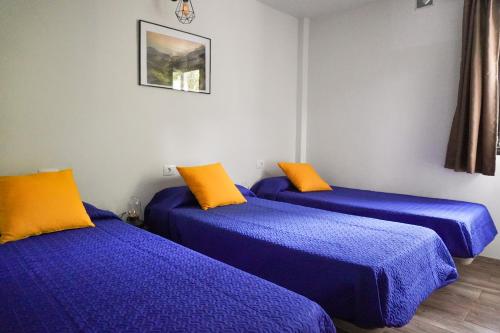 three beds in a room with blue and orange pillows at El Cedro Cottage Home in Hermigua