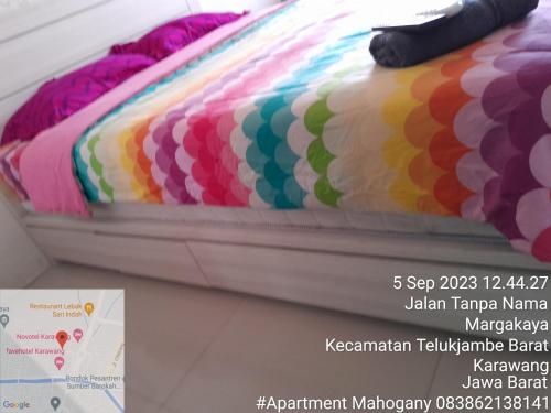 a bed with a colorful blanket on top of it at Tamansari Mahogany Apartment By Sagita Residence Karawang in Karawang
