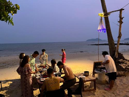a group of people sitting around a table on the beach at Baan AoKao KohMak in Ko Mak