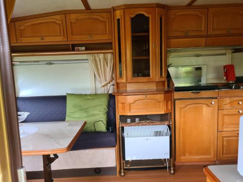 uma cozinha com armários de madeira e um sofá num trailer em Vrijheid caravan em Wallenborn
