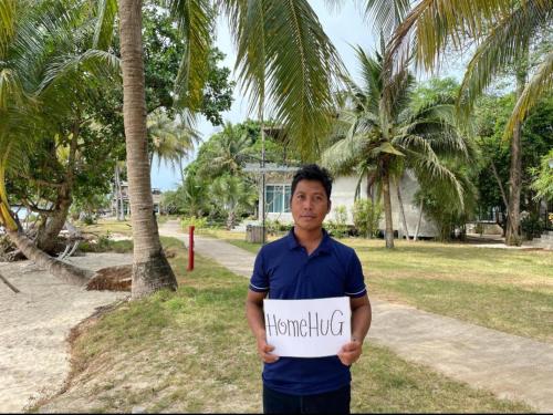 a man holding a sign in a park with palm trees at Baan AoKao KohMak in Ko Mak