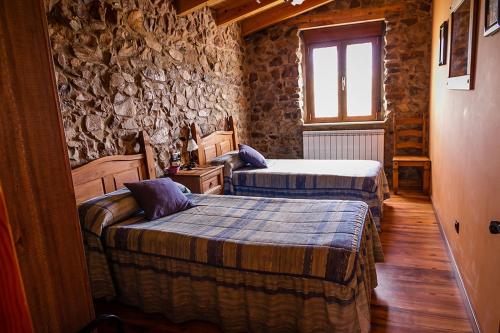 a bedroom with two beds and a stone wall at El Rincón de la Rosa in Brugos de Fenar