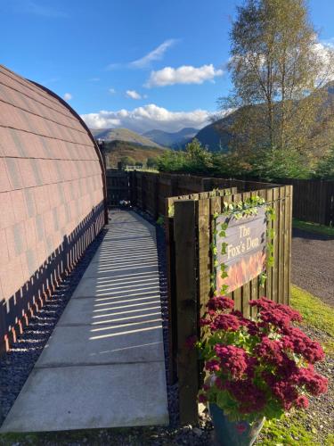 a walkway next to a fence with flowers and a sign at The Fox's Den, Luxury Cosy Mini Lodge, Highlands in North Ballachulish